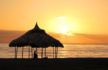 Woman sitting under a cabana on the beach at sunset