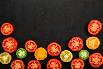 Tomatoes cut in half on the black table, vegetables in the background with space for writing