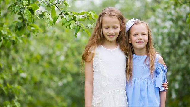 Adorable little girls in blooming apple tree garden on spring day
