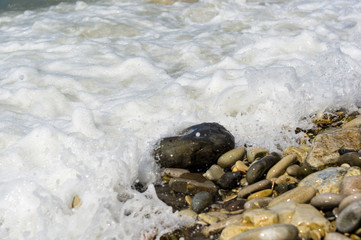 pebble stones on the sea beach, the rolling waves of the sea with foam