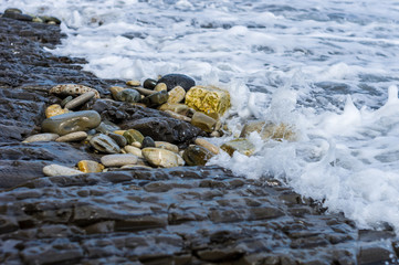pebble stones on the sea beach, the rolling waves of the sea with foam