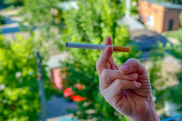 Female hand holding a cigarette on a nature background.