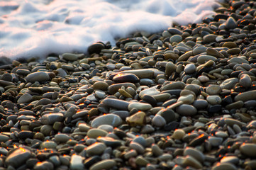 pebble stones on the sea beach, the rolling waves of the sea with foam