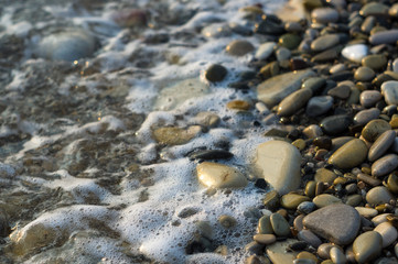 pebble stones on the sea beach, the rolling waves of the sea with foam
