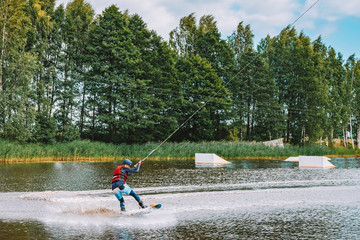 Young man wakeboarding on a lake, making raley, frontroll and jumping the kickers and sliders. Wakeboard.