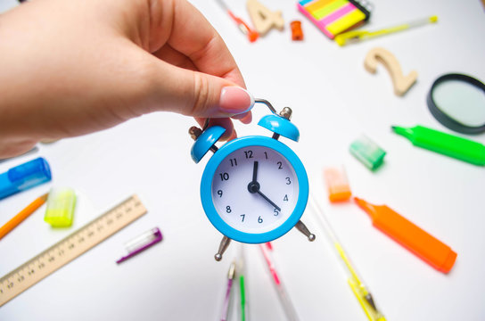 back to school. blue alarm clock on the school desk in the hands of a student. stationery. accessories. White background. stickers, colored pens, pencils, scissors. view from above. flat lay.