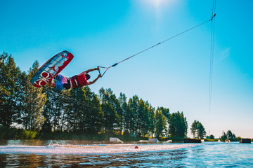 Young man wakeboarding on a lake, making raley, frontroll and jumping the kickers and sliders. Wakeboard.
