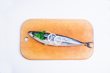 Fresh fish on a wooden board, decorated with rings of onions and greens, top view.