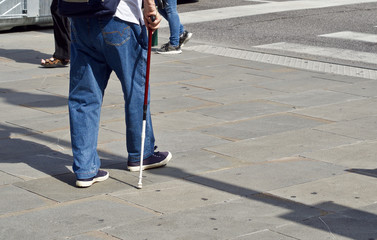 Ein älterer Mann mit einem Gehstock nähert sich einem Schutzweg 