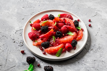 Salad with berries (blackberries and raspberries), grapefruit and pomegranate seeds on grey background. 