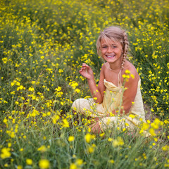 Naklejka na ściany i meble Portrait of happy little girl in field of yellow blossoming arugula. Travel and recreation