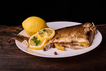 On a wooden table plate with roasted carp fish dorado with parsley, chives and lemon. Concept health food