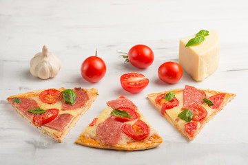 Delicious sliced pizza with tomatoes, mozzarella cheese, basil, and a tomato on a light background,