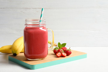 Mason jar with tasty strawberry smoothie on wooden board