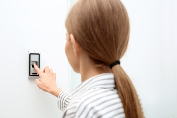 Young woman pressing fingerprint scanner on alarm system indoors