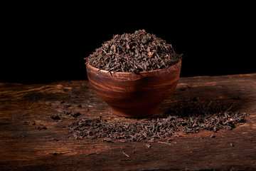 Top view of dried black tea in clay bowl on wooden table. Concept of tea production. Macro, close up
