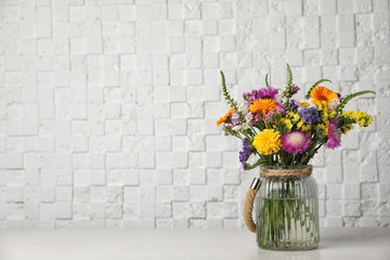 Vase with wild flowers on table near white brick wall