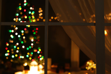 Blurred view of stylish living room interior with Christmas lights at night through window