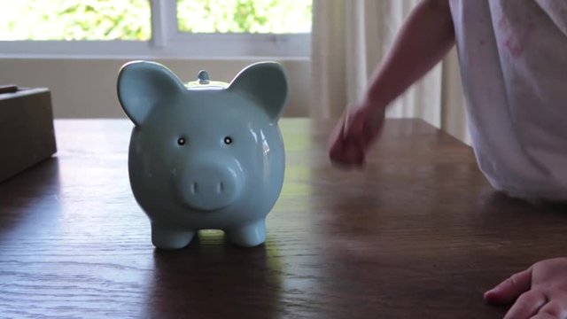 close up footage of a youg childs hand putting money into a blue piggy bank