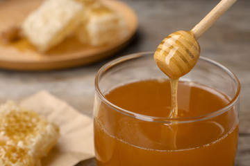 Sweet honey dripping from dipper into glass jar, closeup