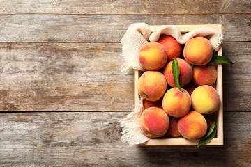 Obraz na płótnie Canvas Wooden crate with fresh sweet peaches on table, top view