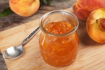Jar with tasty peach jam on wooden table