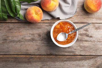 Flat lay composition with bowl of tasty peach jam, spoon and fresh fruit on wooden table