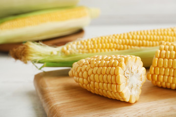 Tasty sweet corn cobs on wooden board, closeup