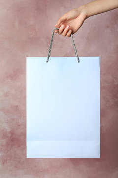 Woman holding paper shopping bag on color background