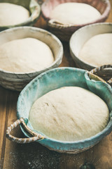 Sourdough for baking homemade wheat flour bread in baskets over rustic wooden kitchen table background, selective focus, vertical composition