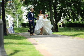 back groom and bride walking along the alley on the background of trees