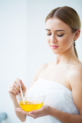 Women hold orange paraffin wax bowl. Woman in beauty salon