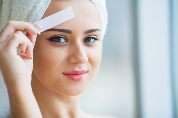 Beautician waxing young woman's eyebrows in spa center