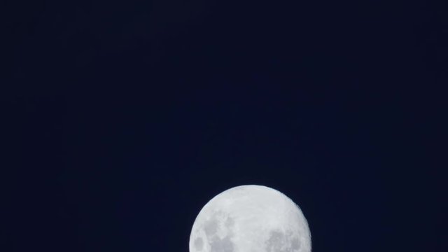 Full moon rising from out of frame against deep blue night sky.
