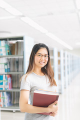 Asian Woman holding a book at bookshelf in the library..