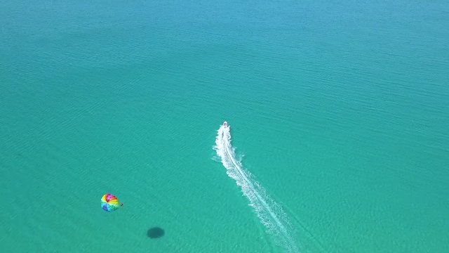 Parasailing in blue sea drone view. Parasailing summer activity and extreme entertainment while resting on resort beach. Colorful parasail wing pulled by sea boat in the sea water aerial view.