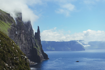 Beautiful view of Trollkonufingur (Witch's Finger) Fjord appear from clouds in blue sky next to North Atlantic ocean, hiking from Sandavagur village on Vagar island of the Faroe Islands