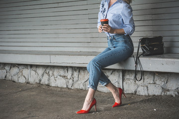 Girl in red shoes and blue jeans sitting on the banch and drinking coffee 
