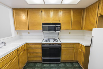 Old condo kitchen with oak cabinets, tile countertops, gas stove and green vinyl flooring. ...