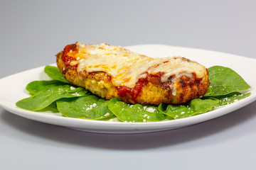 Chicken Parmesan on a bed of spinach with a sprinkle of fresh parmesan cheese on top on a white...
