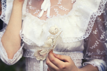 Young virgin girl in a white lace wedding dress holding a flower. Tender delicate woman at a wedding