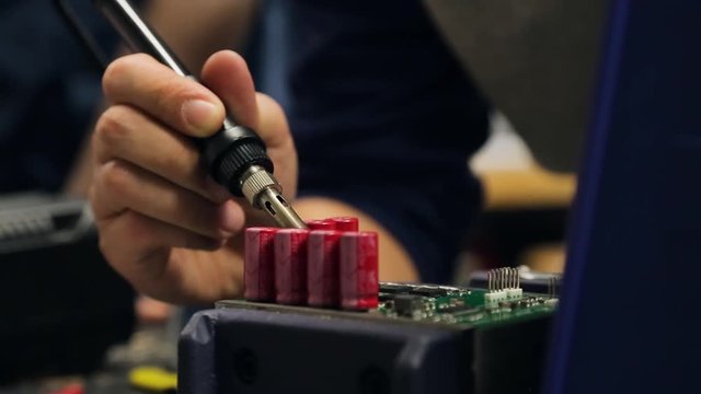 A college engineering student soldering a circuit board with several capacitors.