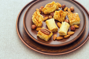 Middle east dessert  with honey syrup and chopped nuts in a clay flat round plate. Traditional honey sweets close up. Selective focus.