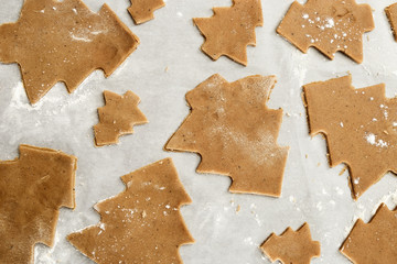 Gingerbread Cookie. New Year figures from a dough, prepared for baking in the oven. Biscuits in the form of a Christmas tree on paper for baking. Raw biscuit cookies.