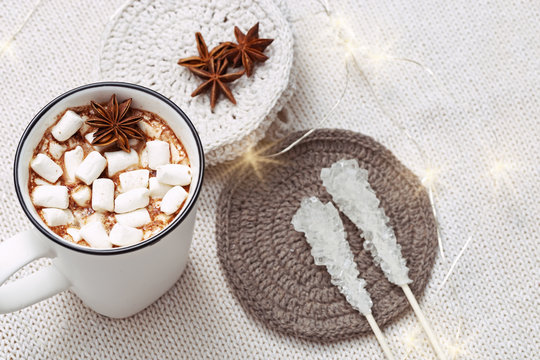 Hot chocolate or cocoa with marshmallows  with cozy soft knitted fabric decorated lights. Holiday concept. Selective focus. Copy space.