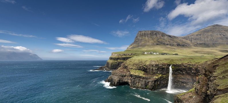Cliffs with a waterfall near a village, Mykines Island at the rear, Gasadalur, Vagar, Faroe Islands, Denmark, Europe