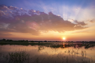 Sunset reflect on water at lake farm field landscape and sun flare with cloudy twilight sky background