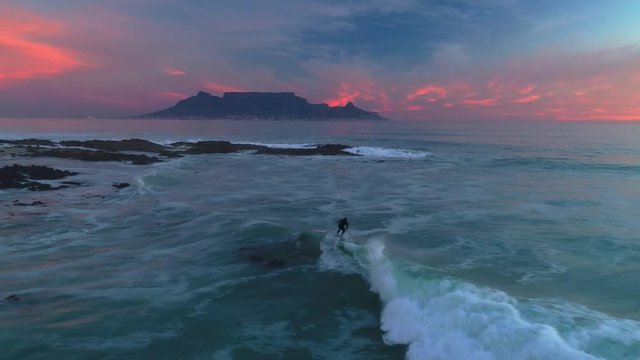 Stand up paddle board surfing a perfect wave during a beautiful sunset at Big Bay, Bloubergstrand, Cape Town, South Africa. Table Mountain in the background. Aerial view, shot with drone.