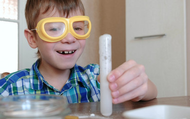 Experiments on chemistry at home. Smiling boy is looking at chemical reaction with the release of...