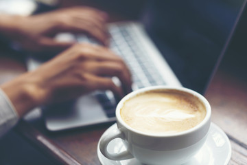 Businessman using laptop with tablet and pen on wooden table in coffee shop with a cup of coffee